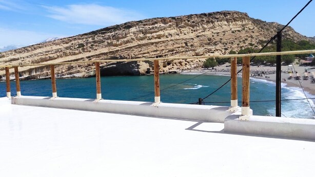 Cubierta de barco con barandilla de madera que da a una zona costera con acantilados y una playa.