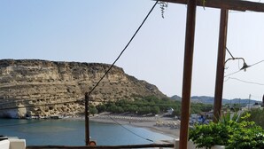 Una terraza con dos sillas naranjas y una mesita, con vistas a una zona costera con acantilados y una playa.