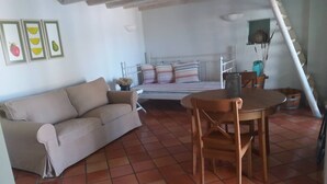 Una habitación acogedora con sofá, cama con ropa de cama a rayas, una mesa de madera y suelo de baldosas.