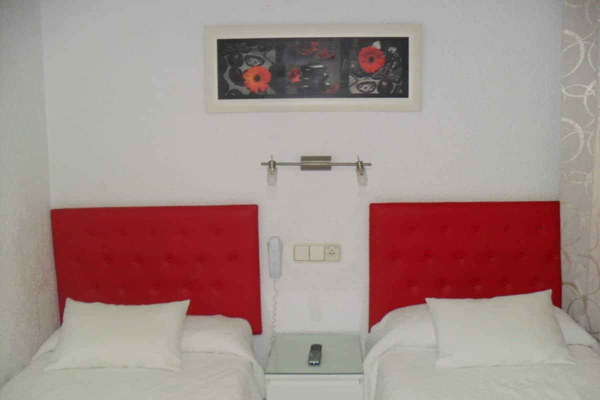 Ett hotellrum med två sängar, var och en med en röd sänggavel, vita sängkläder och ett litet nattduksbord med en telefon.