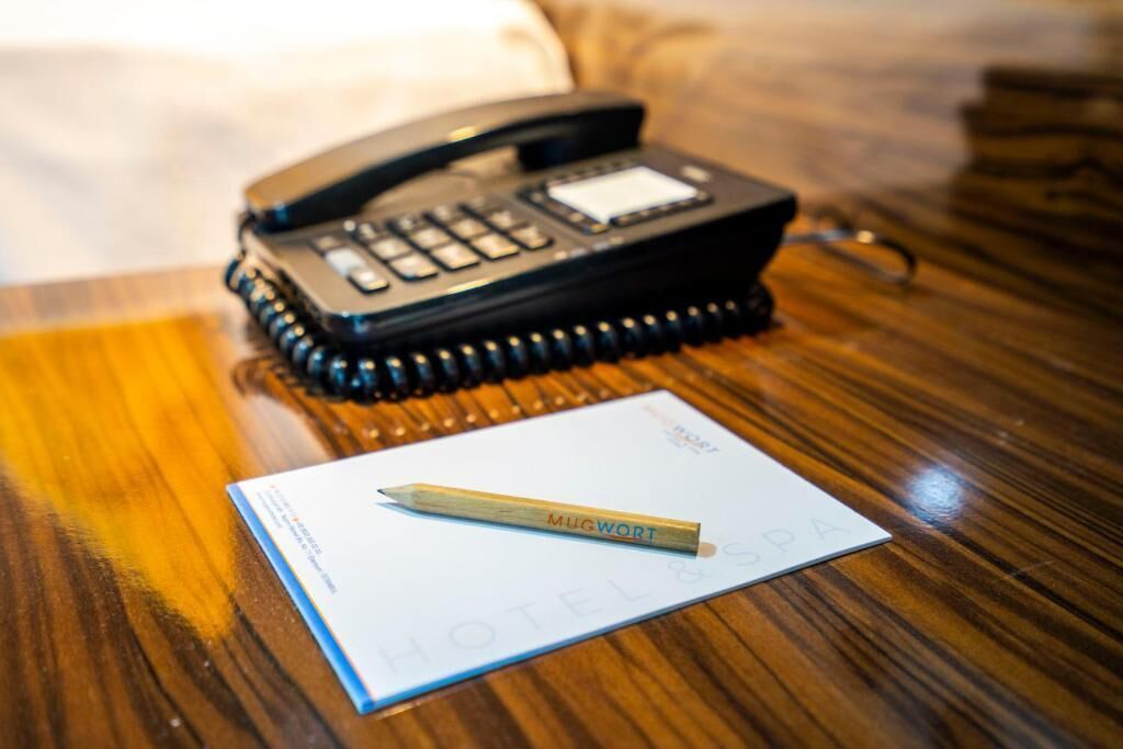 A hotel room with a wooden table, a black telephone, and a notepad with a pencil.