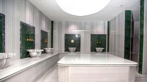 Uma casa de banho moderna com uma ilha central, paredes de mármore e detalhes em dourado.