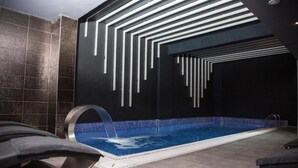 Piscina interior moderna com design de parede geométrico, elemento aquático e chão revestido.
