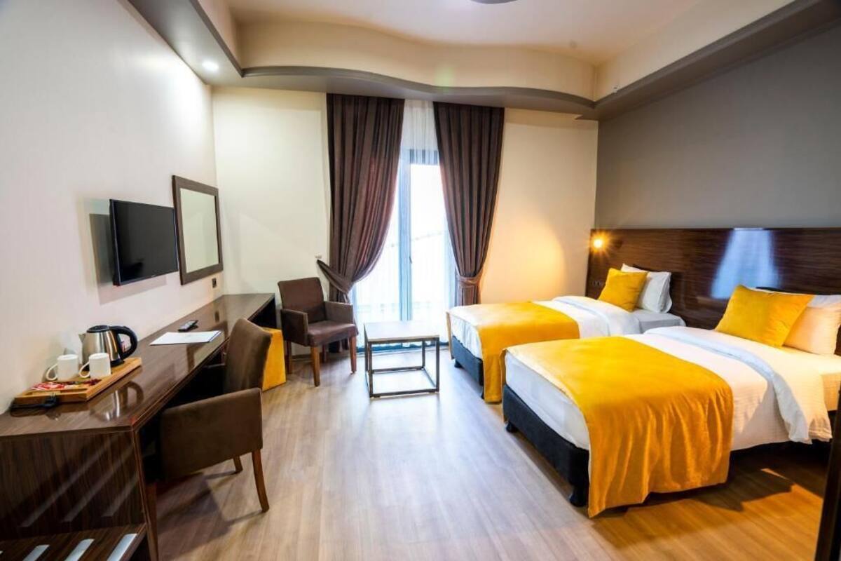 Hotellihuone, jossa on kaksi sänkyä, työpöytä, tuoli, televisio ja ikkuna, jossa on verhot.