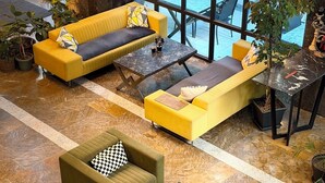 A spacious indoor seating area with multiple sofas and tables, surrounded by large windows and potted plants.