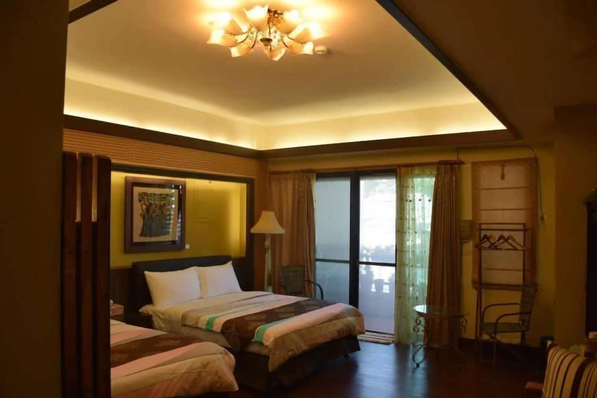 A hotel room with two beds, a chandelier, a balcony with a table and chairs, and a view of the city.