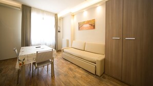 Um quarto com piso de madeira, um sofá bege, uma mesa de jantar com cadeiras e um guarda-roupa grande.