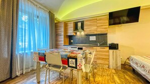 Quarto de hotel compacto com cozinha compacta, uma mesa de jantar com cadeiras, uma cama e uma televisão fixada na parede.