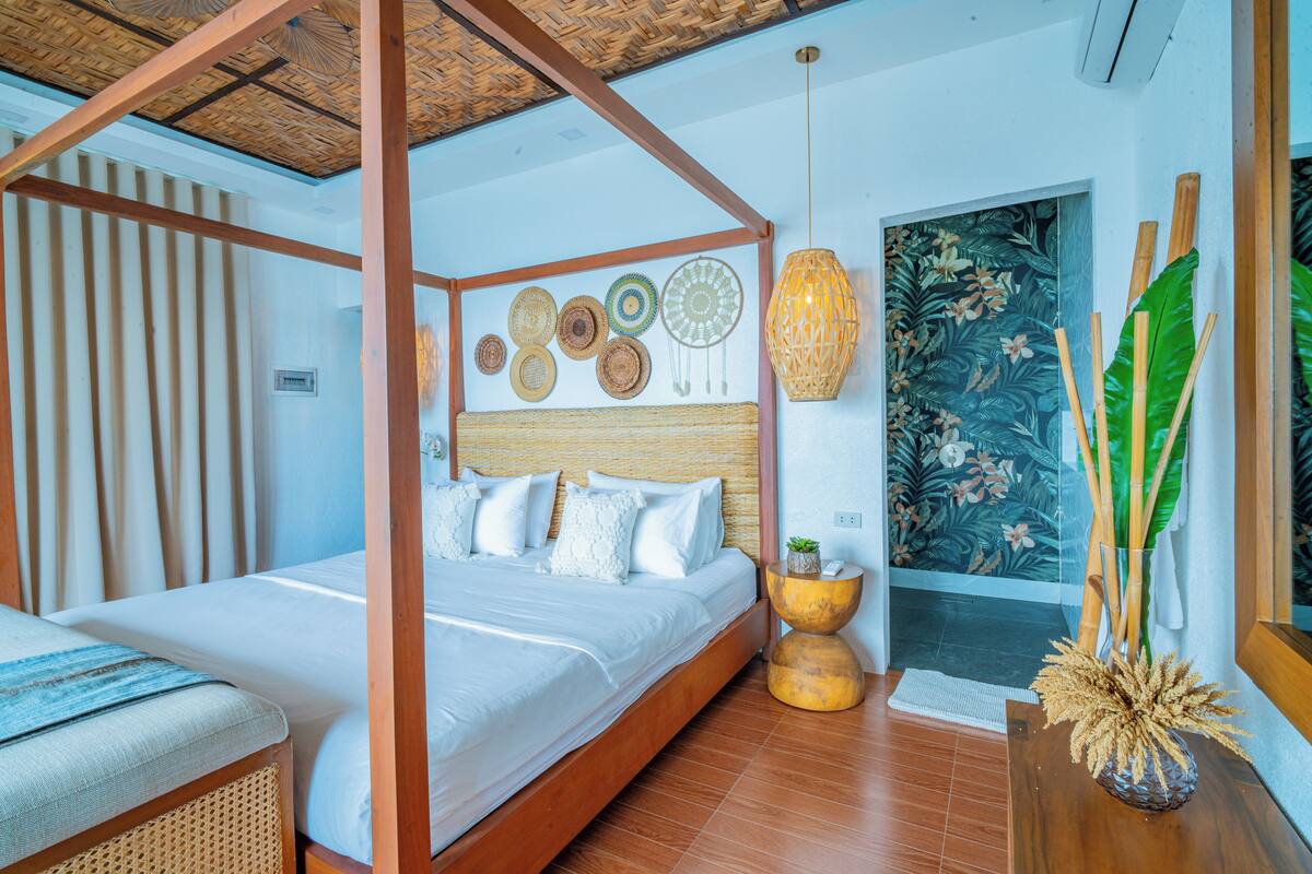 A four-poster bed with a woven headboard, a woven bench, and a wall decorated with woven mats and dreamcatchers.