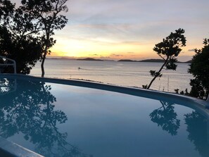 Une piscine offrant une vue sur la mer et les îles lointaines au coucher du soleil.