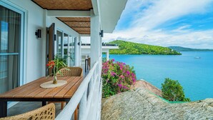 Un balcone con un tavolo in legno, sedie in vimini e vista su un lago con barche.