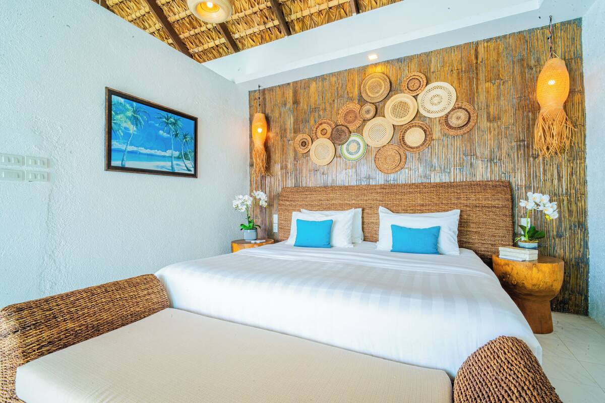 A large bed with white and blue bedding, a woven headboard, and a wall decorated with woven circular patterns.