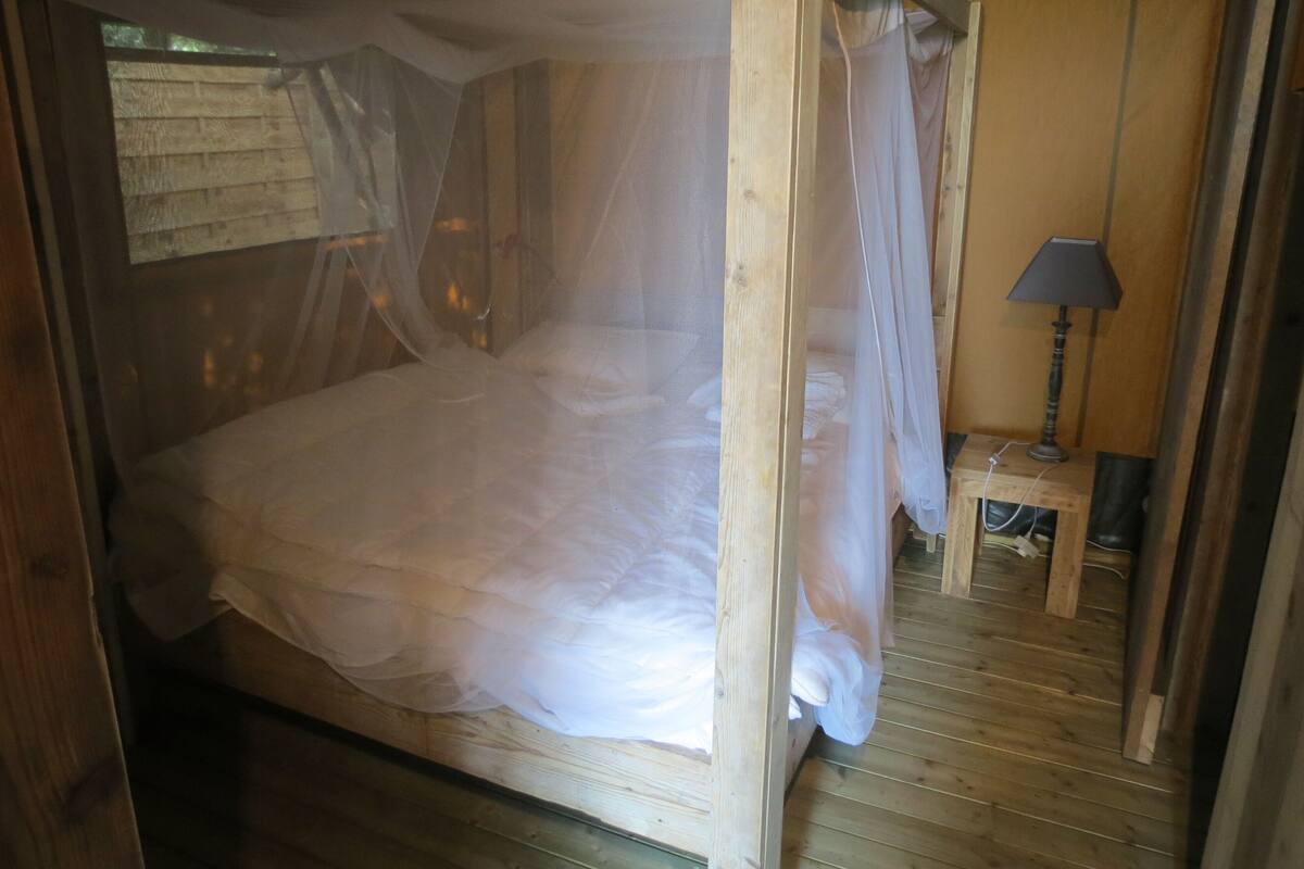 A wooden four-poster bed with a canopy, a bedside table with a lamp, and a wooden floor.