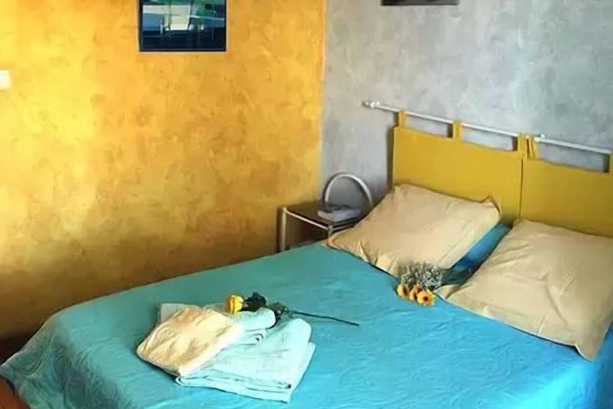 A bedroom with a bed, a bedside table, a lamp, and a painting on the wall.