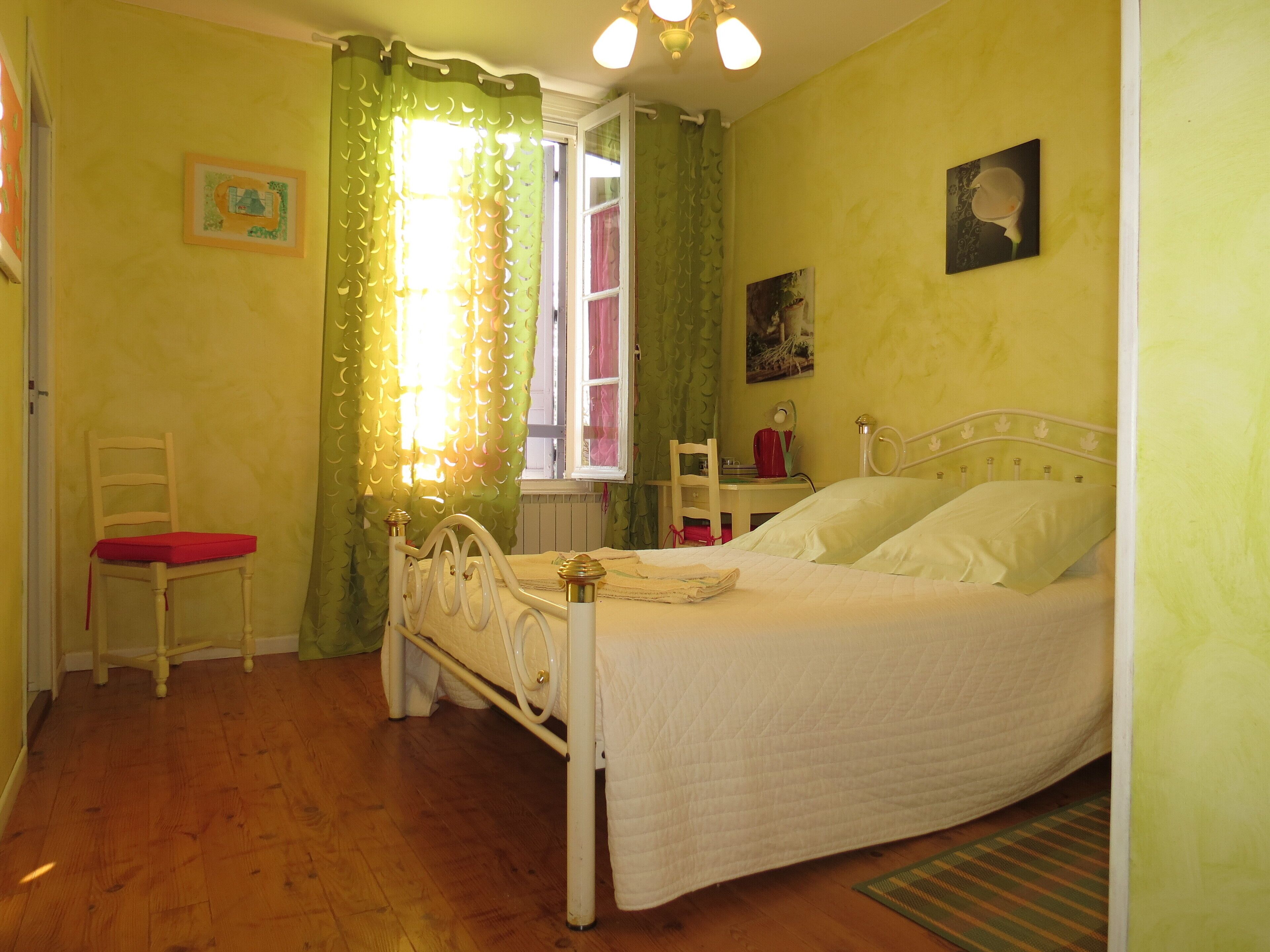 A bedroom with a single bed, a chair, a desk, and a window with curtains.