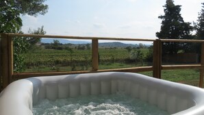 An inflatable hot tub with a view of a vineyard and distant hills. - Domaine du Siestou Wine Resort & Spa (Laure-Minervois)