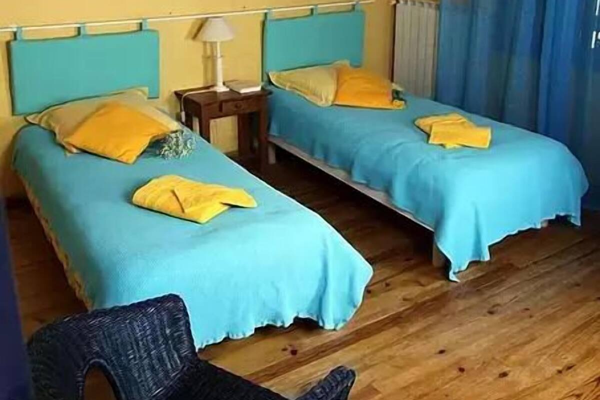 A room with two beds, a chair, a lamp, and a wall art piece.