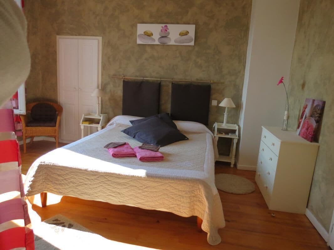 Une chambre à coucher avec un lit, une chaise, une commode et un tableau accroché au mur.
