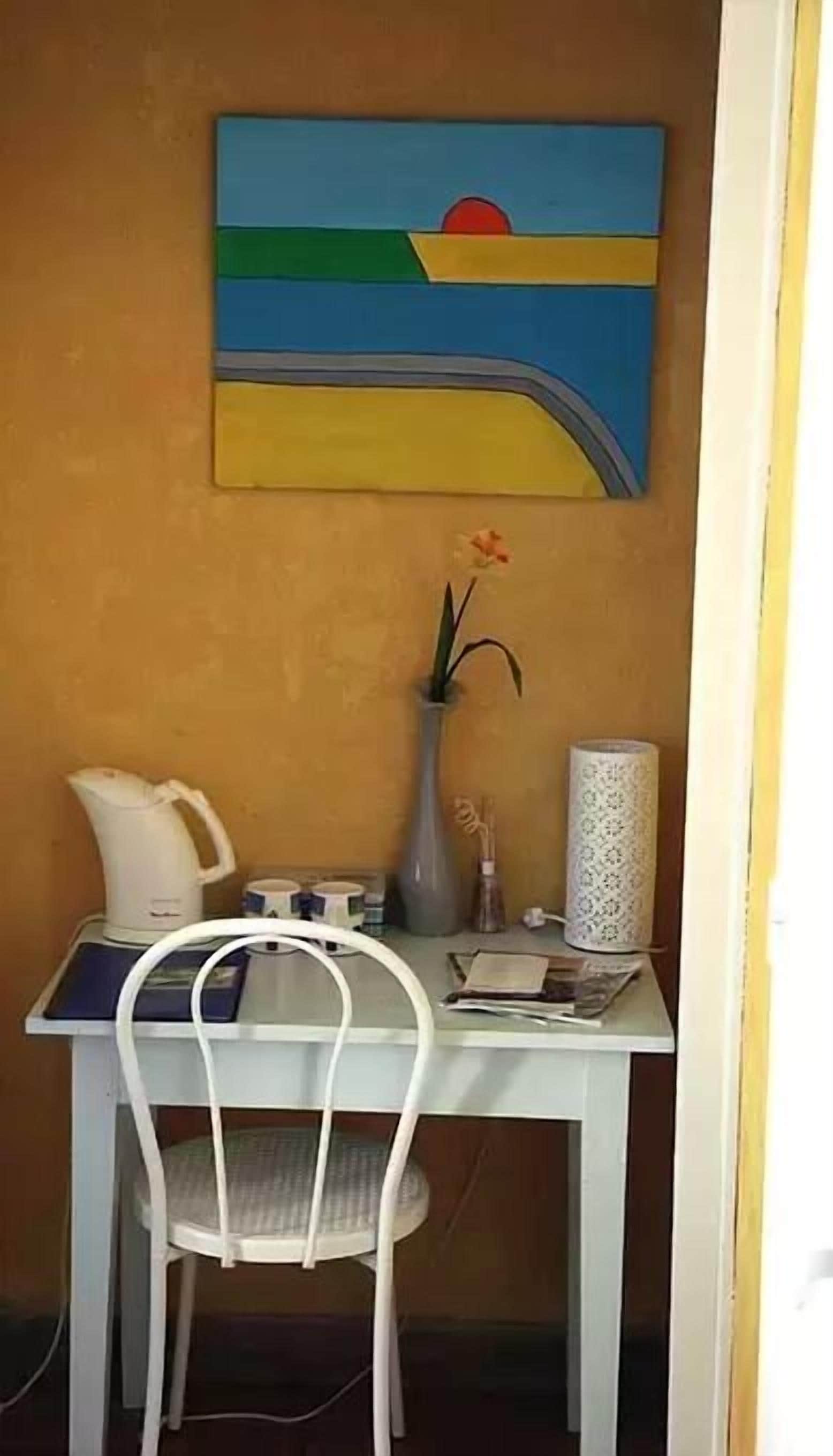 Un petit coin repas avec une table, une chaise, un vase de fleurs, une machine à café et un objet décoratif accroché au mur.