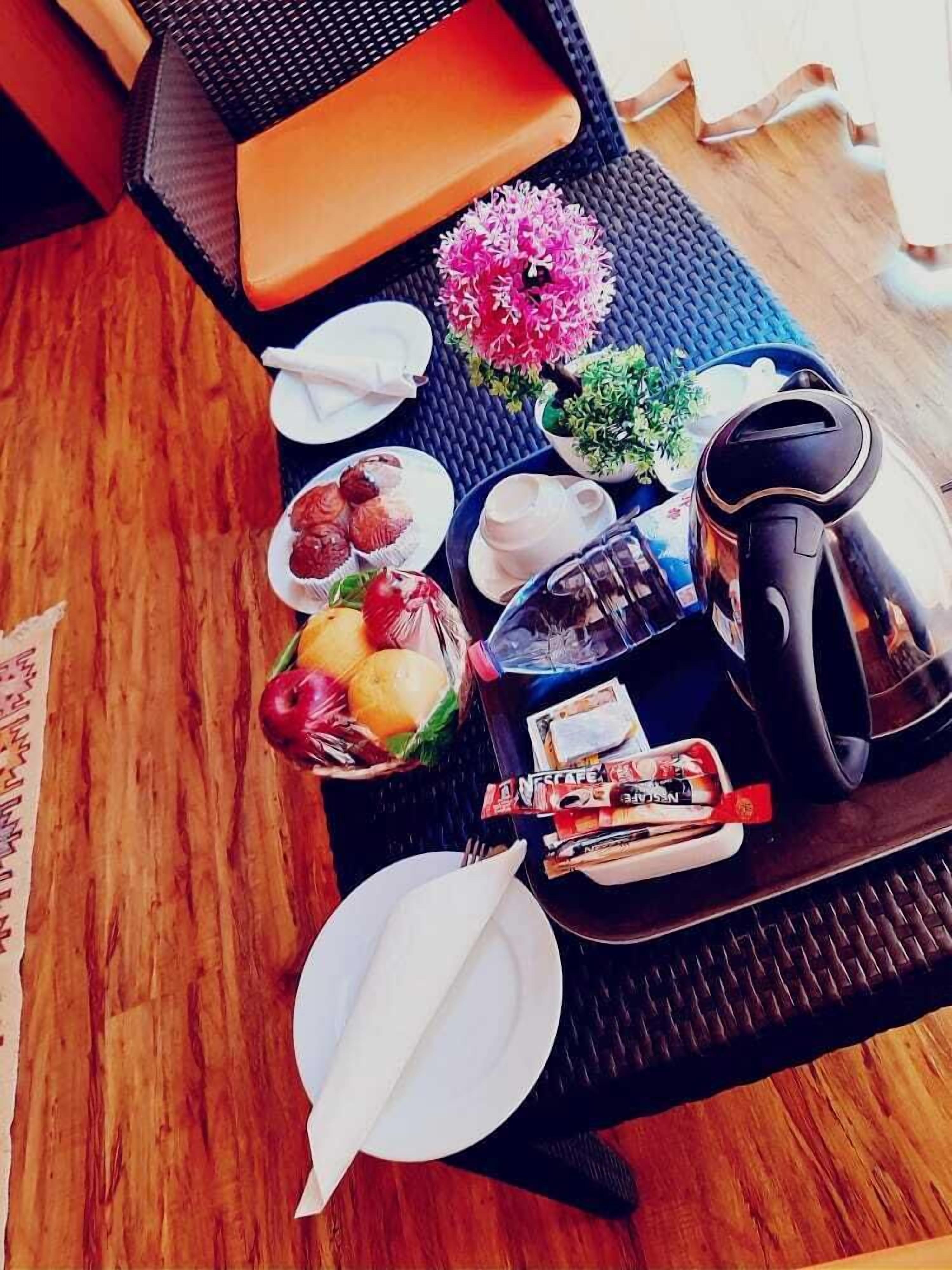 A breakfast tray with a coffee maker, a bowl of fruit, a plate of pastries, and a small vase with flowers.