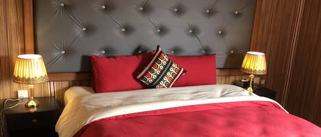 A bedroom with a tufted headboard, red bedding, two bedside lamps, and an air conditioning unit.