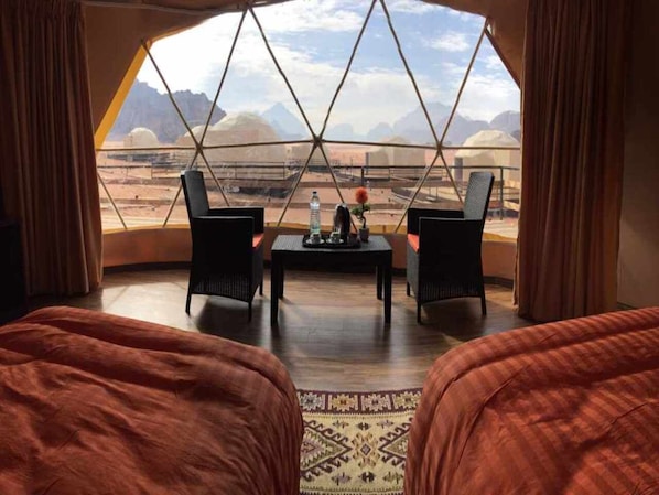 A room with two beds, a table, and two chairs facing a large window with a mountain view.