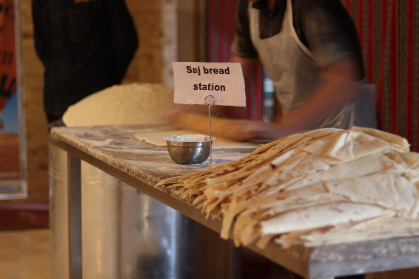 A bread station with a sign, a metal bowl, and a person in the background.