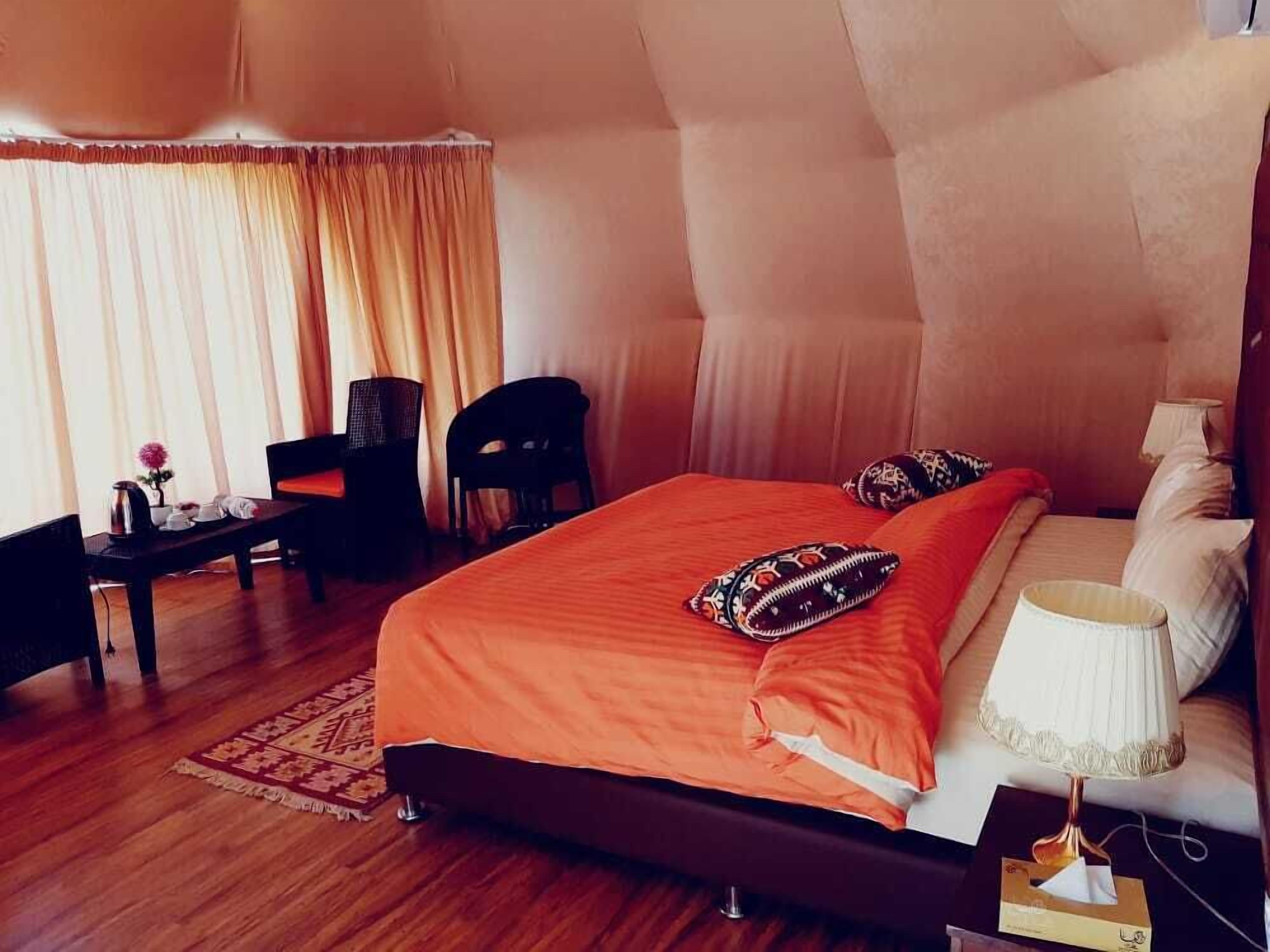 A bedroom with a large bed, a desk, a chair, and a window with curtains.