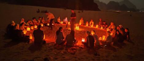 Un groupe de personnes assises autour d’un feu de camp sur une plage, la nuit.