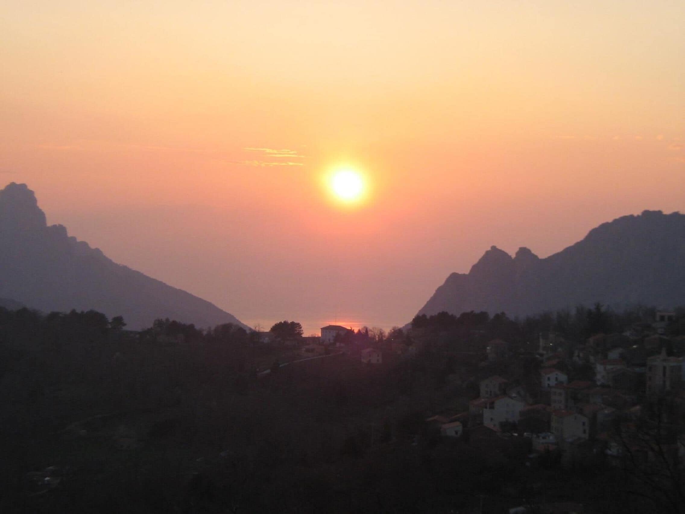 A sunset over a mountainous landscape with a town in the foreground.