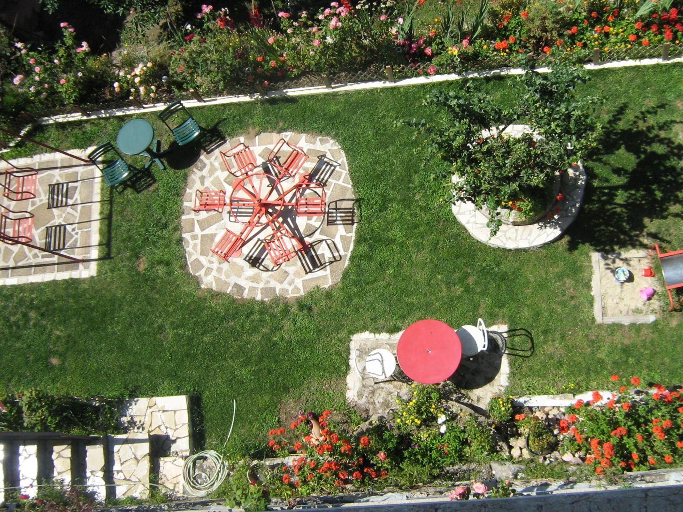 Un espacio de estar circular al aire libre con una mesa central y sillas, rodeado por un jardín con diversas plantas y flores.
