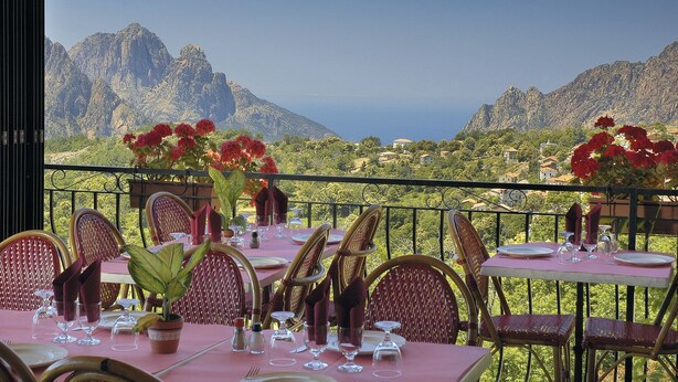 A dining area with tables set for two, overlooking a mountainous landscape. - Hotel Aitone (Evisa)