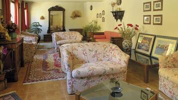 A living room with floral-patterned sofas, a glass coffee table, and a variety of decorative items including a mirror, plants, and framed pictures on the walls.
