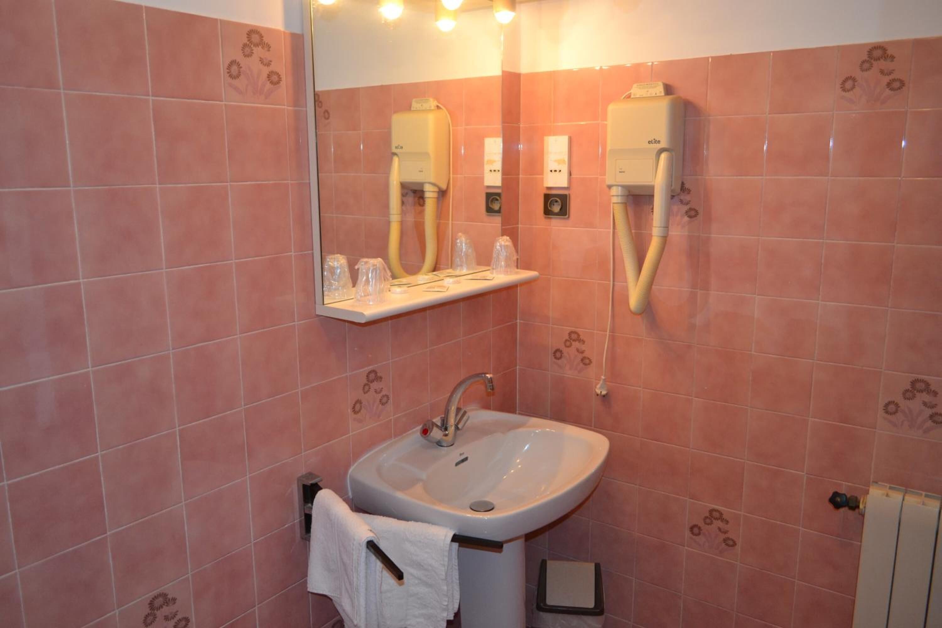 Un baño con azulejos rosados, un lavamanos, un espejo y dos dispensadores de toallas.