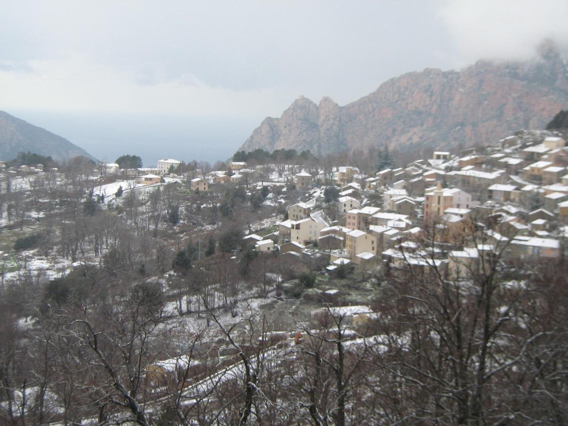 A town with buildings surrounded by mountains and snow-covered roofs.