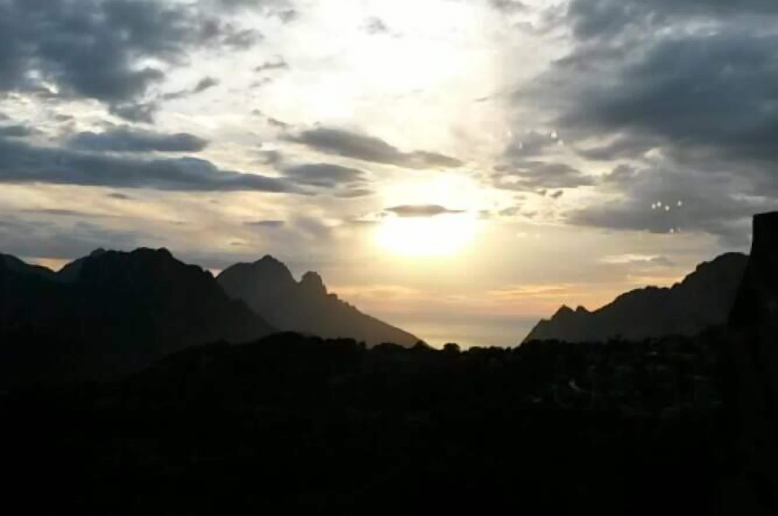 A mountain landscape with a sun setting or rising behind the peaks.