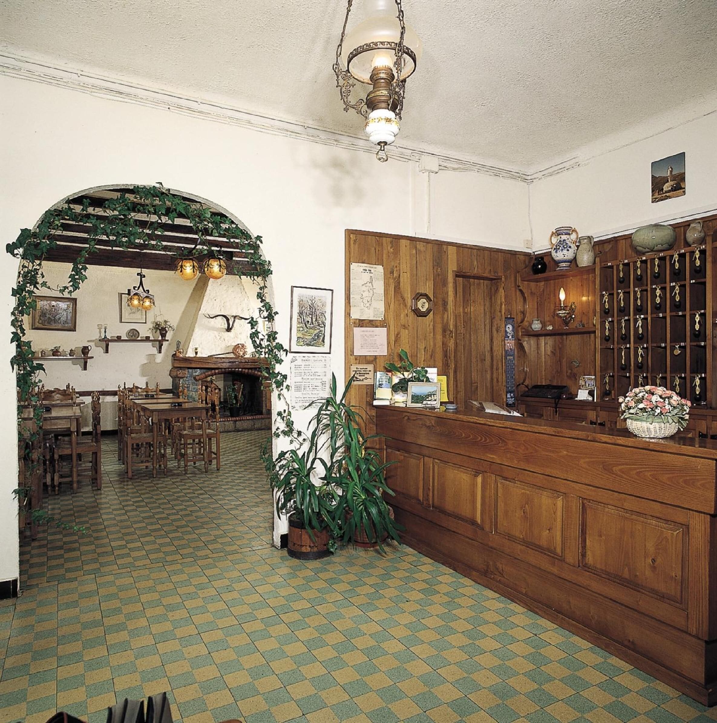 Una stanza accogliente e ben illuminata, con una reception in legno, un pavimento piastrellato e un arco verde che conduce a una sala da pranzo con arredi in legno.