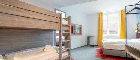 A modern hotel room with bunk beds, a large window with yellow curtains, and a red carpet.