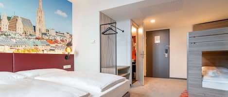 Une chambre d’hôtel avec un grand lit, une armoire, un miroir et une vue sur une fresque représentant un paysage urbain.