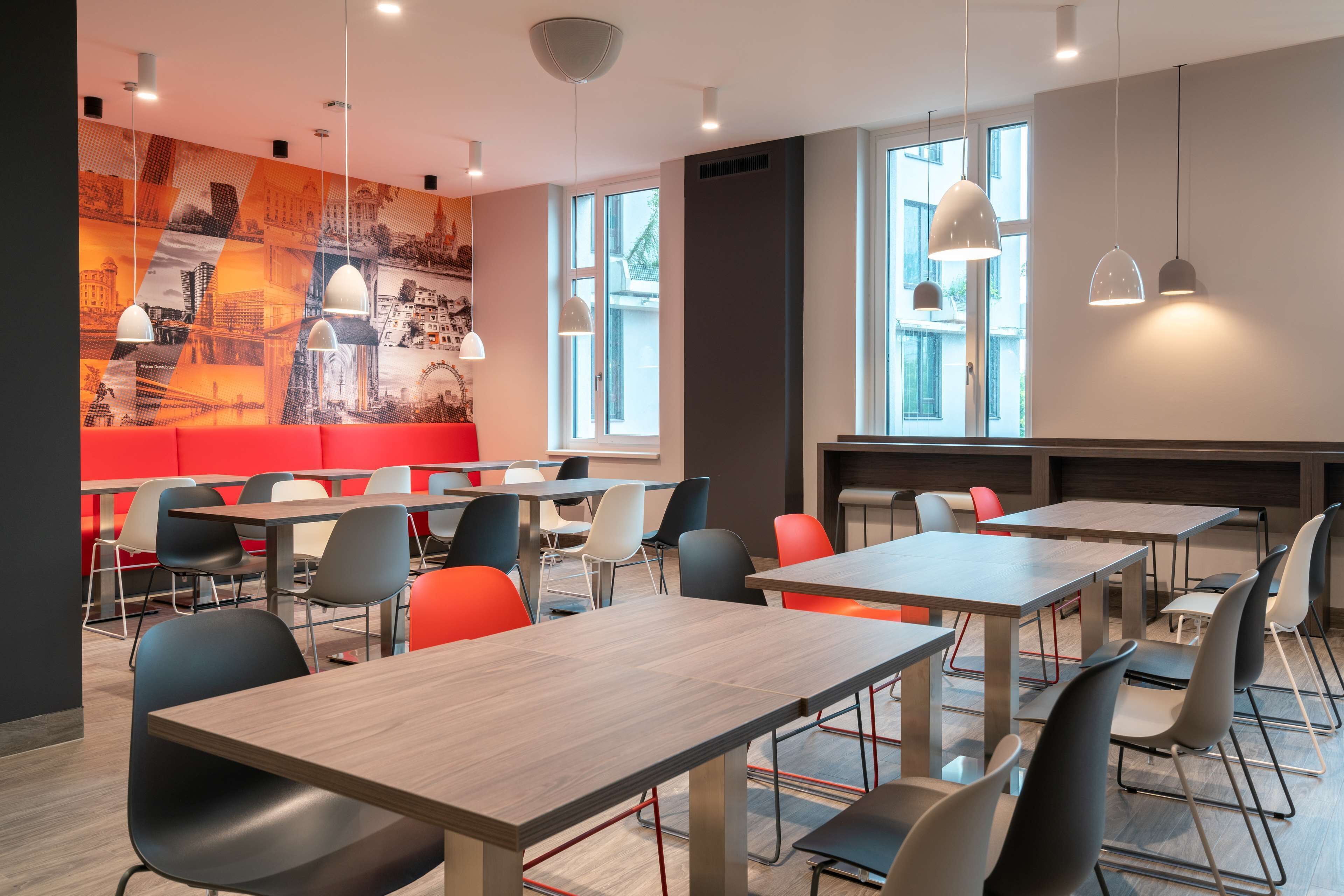 A modern dining area with tables and chairs, a red seating area, and large windows.