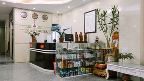 A hotel reception area with a glass display of toiletries, a reception desk, clocks showing different time zones, and a large framed document on the wall. - Tuan Anh Hotel (Hanoi)