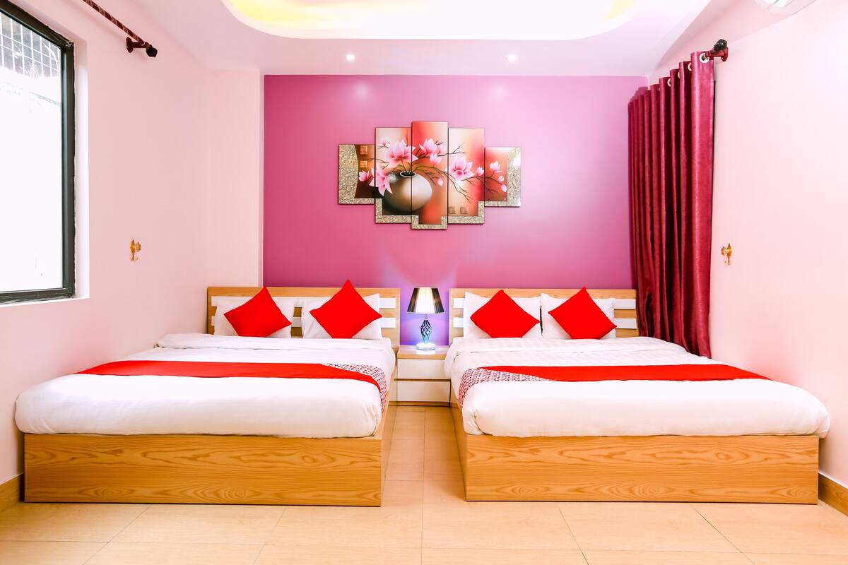 Een hotelkamer met twee bedden, een roze muur en een grote bloemenprint boven de bedden.