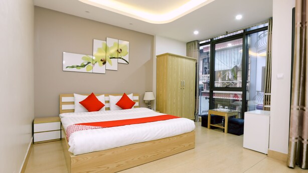 A modern bedroom with a wooden bed, red pillows, and a red bedspread. There is a wardrobe, a small table, and a view of the outside through a glass door. - Tuan Anh Hotel (Hanoi)