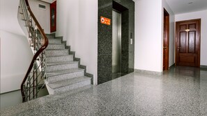 A clean, modern lobby with a marble staircase, a fire safety sign, and a wooden door. - Tuan Anh Hotel (Hanoi)
