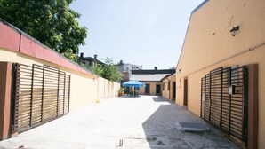 A narrow alleyway with closed metal gates on both sides, leading to a building with a blue umbrella and a sign. - Casa Stefan Galati (Galati)