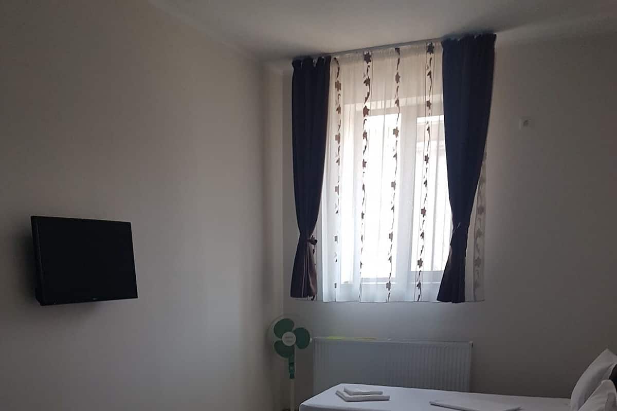 A hotel room with two single beds, a flat-screen TV mounted on the wall, a radiator, and a window with curtains.