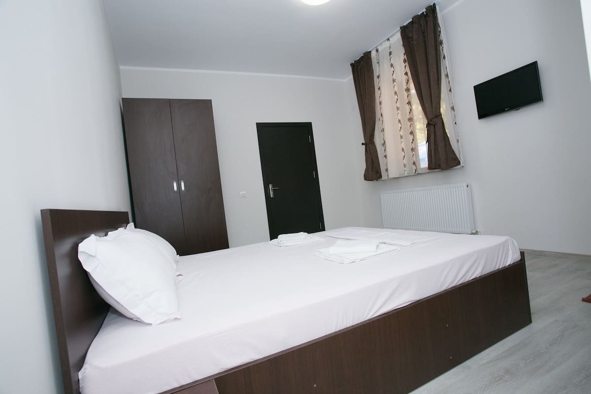 A bedroom with a bed, a wardrobe, a door, a radiator, and a TV on the wall.