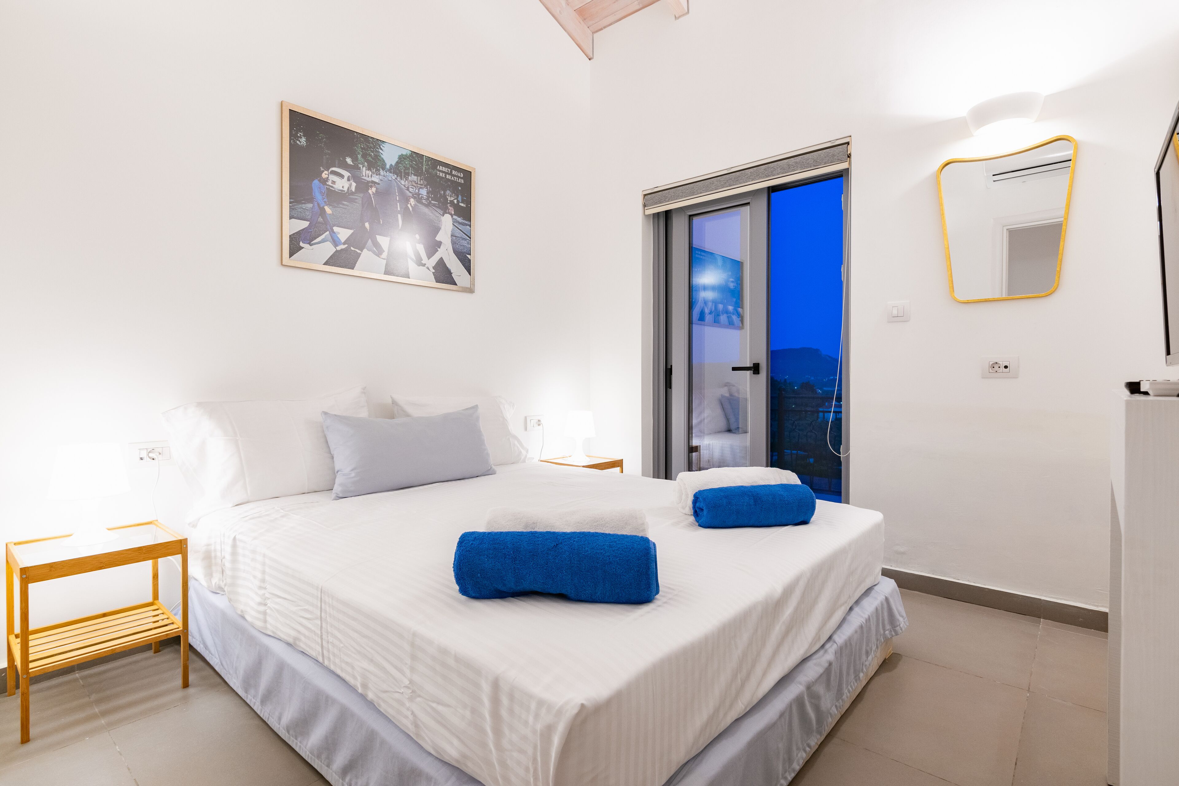 Ein Schlafzimmer mit einem großen Bett, einem Nachttisch, einem Spiegel und einer Tür, die auf einen Balkon führt.