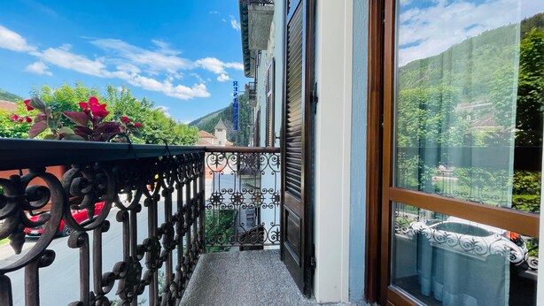 Uma varanda com guarda-corrimão de metal, vista para uma montanha e um edifício com uma placa ao fundo.