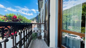 A balcony with a metal railing, a view of a mountain, and a building with a sign in the background. - TABOR - CLASSIC ONE-BEDROOM APARTMENT sleeps 5 (Bardonecchia)